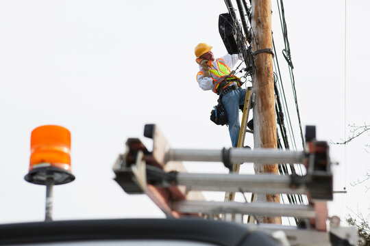 Communications worker talking on butt set while installing new cables on power pole