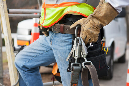 Power line worker with tool belt and safety harness at his truck