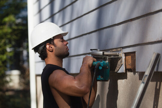 Hispanic carpenter trimming house siding for installation of new deck
