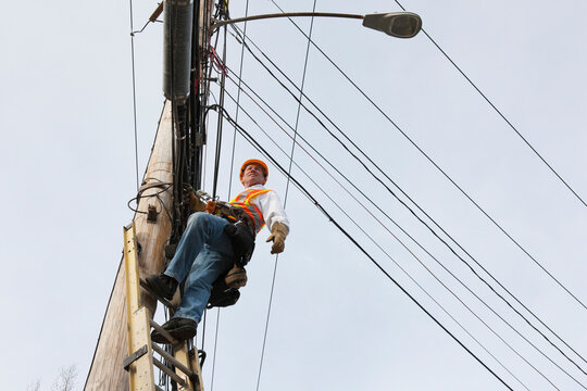 Communications worker standing on ladder on power pole