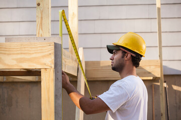 Hispanic carpenter measuring deck joist using retractable ruler