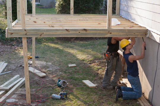 Hispanic carpenters nailing joist supports for deck construction