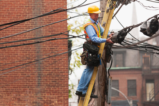 Cable lineman assessing a weather proofing boot for suspended wire connections in the city