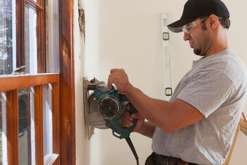 Hispanic carpenter using circular saw to cut wallboard for deck doorway in house