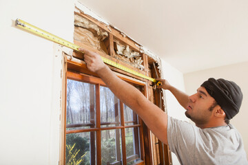 Hispanic carpenter measuring framing over window during home renovation