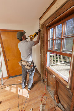 Hispanic carpenter using reciprocating saw to remove window and cut access doorway