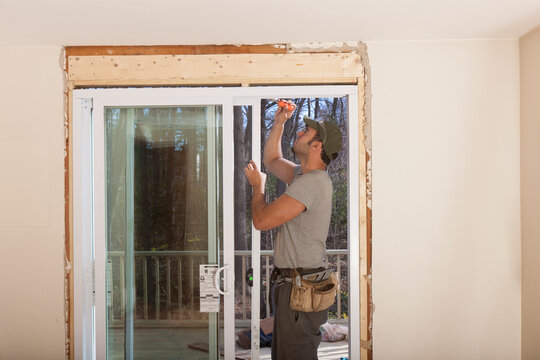 Hispanic carpenter installing glass doors in new door frame for deck access on house