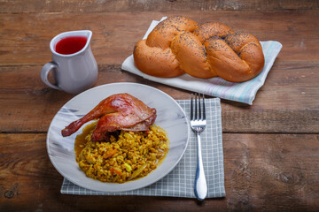 Spelled with vegetables and a duck leg in a light plate next to it on a napkin on the table next to the challah and a jug of wine.