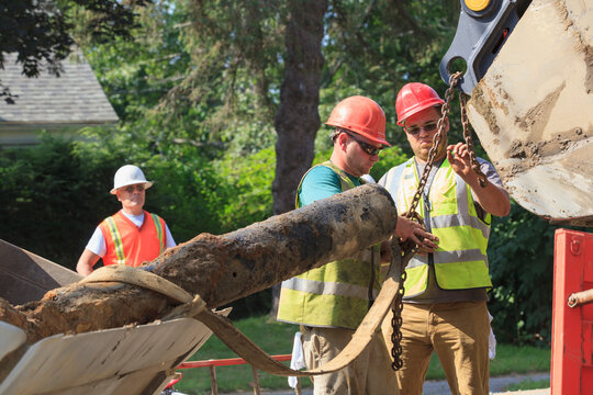 Construction workers unhooking old watermain from excavator