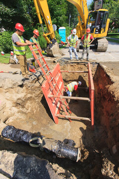 Construction workers measuring length of pipe while protected by shoring