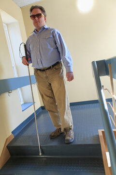 Man with congenital blindness using his cane to go down a stairwell
