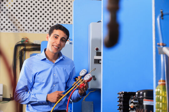 Student demonstrating air conditioner recharging manifold with gauges in HVAC classroom