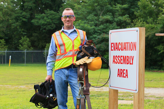 Communications engineer with climbing equipment and tool belts at evacuation assembly area