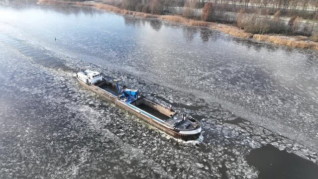 Freight ship barge ploughing through ice on a froze Drontermeer lake during a cold winter day in The Netherlands