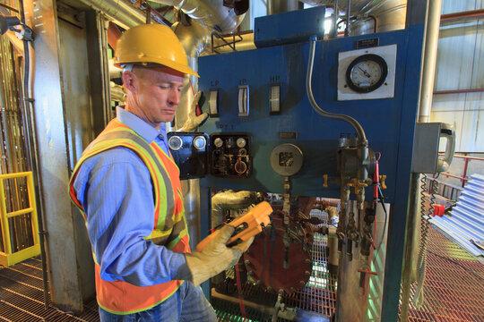 Worker wearing hard hat and reflective vest using equipment with gauges and monitors