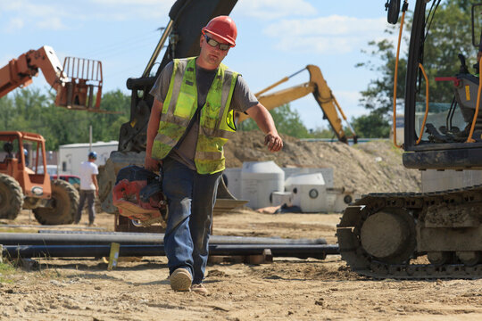 Construction engineer carrying pipe cutting saw at heavy construction site with excavator