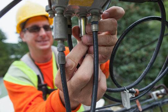 Cable lineman attaching a line filter at a junction box from a bucket truck