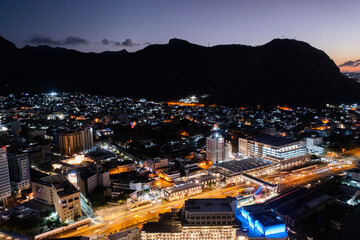 Aerial night view of the old and modern buildings at Waterfront in Port Louis, Capital of Mauritius with  Bird eyes view during nighttime, with illuminated buildings in front and dark mountain scenery