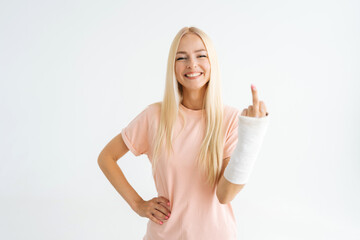 Happy injured young woman showing middle finger, rude gesture with broken arm wrapped in plaster...
