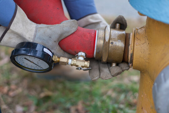 Gloved hands attaching hose with pressure gauge to fire hydrant