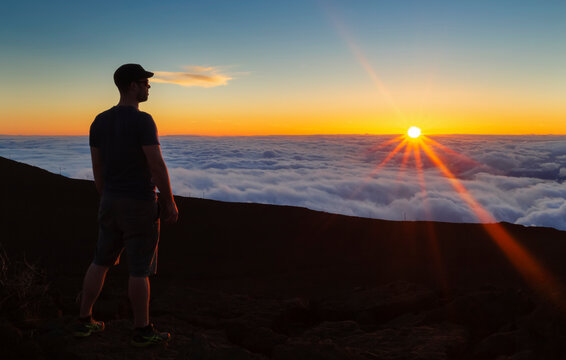Silhouetted man standing on rock above the clouds at sunset, Haleakala; Maui, Hawaii, United States of America