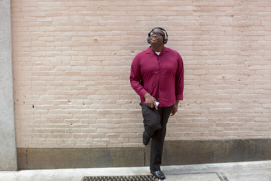 Man with ADHD standing against a wall listening music