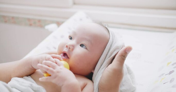 Portrait close up shot of little cute Asian newborn baby in a white bathrobe smiling relaxing lying on the table, Dad hands wipes his adorable little child after bathing, healthcare parenthood concept