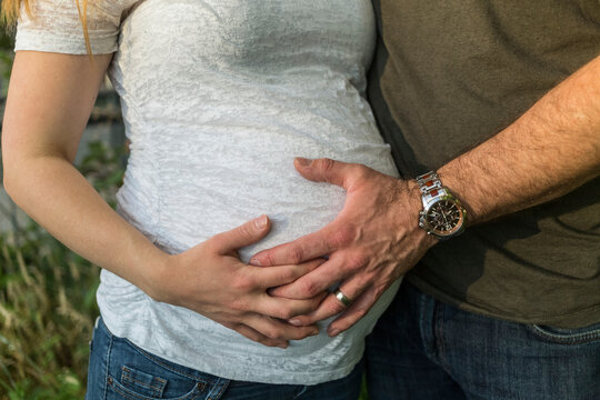 Man and woman's hand on full-term pregnant belly; Vancouver, British Columbia, Canada