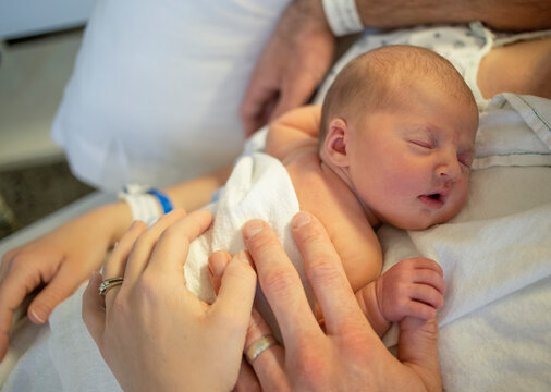 Newborn baby sleeping on mother's chest in a hospital bed with mother and father's hands visible; Vancouver, British Columbia, Canada