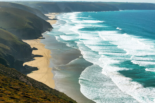 Sandy beaches with surf along a grassy cliff shoreline with blue sky and clouds; Cornwall County, England