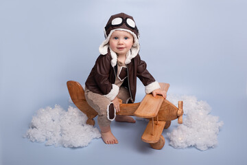 One year birthday party decorations. Little boy in helmet and glasses with wooden plane against the background of a blue wall. Happy child playing with toy wooden airplane. blue background