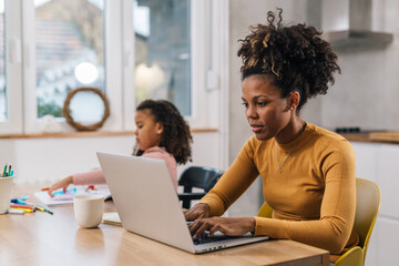 Mom is working from home with her daughter sitting next to her - Powered by Adobe