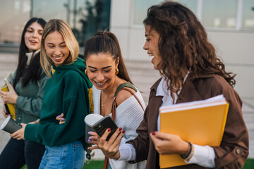 Four college friends look at the phone and laugh