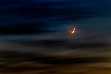 Crescent moon glowing around colourful clouds at sunset; Calgary, Alberta, Canada