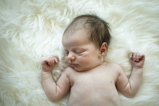 A sleeping newborn baby girl lying on a white fur rug; Studio