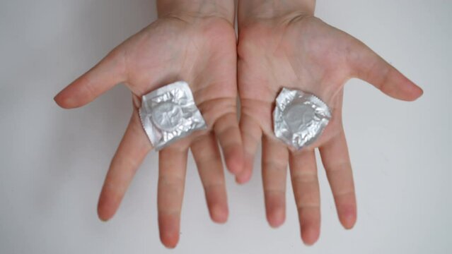 Top view female fists with monkey pox rash turning opening palms with condoms. Unrecognizable ill young Caucasian woman advertising sex STI protection. Slow motion