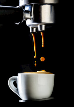 Close up of espresso coffee machine dripping coffee into white espresso cup with foam on surface of cup; Studio