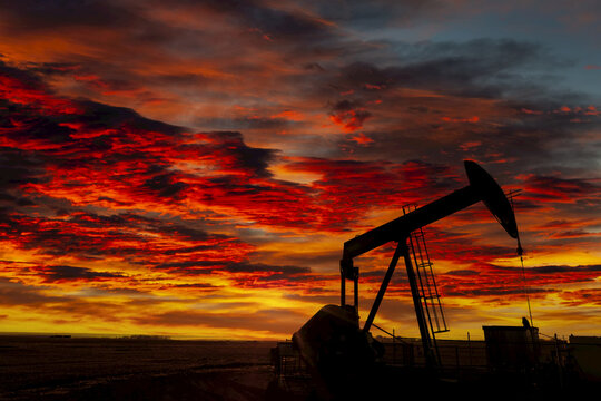 Silhouette of a pumpjack against a colourful dramatic sky and clouds at sunset, West of Airdrie; Alberta, Canada