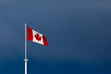 Canadian flag on a white flag pole flying in a blue sky; Surrey, British Columbia, Canada