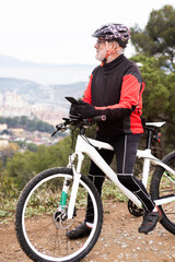 older male cyclist looking at mobile phone to position himself on the bike, equipment and helmet