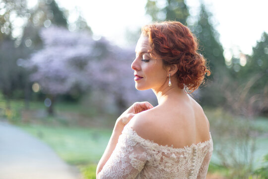 Portrait of a bride with red curly hair and lace gown standing outdoors; British Columbia, Canada