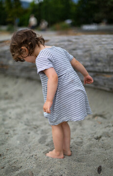 Preschooler girl standing on a beach digging her toes into the sand, Ambleside Beach in West Vancouver, BC, Canada; West Vancouver, British Columbia, Canada