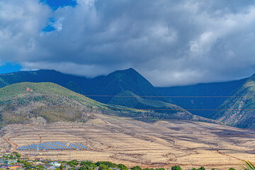Solar panels and power lines on the mountainside over the rooftops of Lahaina Town under a stormy sky; Maui, Hawaii, United States of America