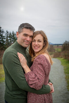 Mid adult couple stand outdoors in a park in a playful affectionate embrace; Aldergrove, British Columbia, Canada
