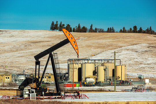 Pumpjack and compressor station against a snow-covered hillside with blue sky, North of Longview, Alberta; Alberta, Canada