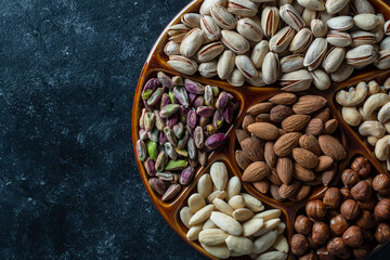 Assortment of nuts in ceramic bowl on a black background, close up, top view, copy space. Cashew, hazelnuts, pistachios and almonds nuts. Vegetarian meal. Healthy eating concept