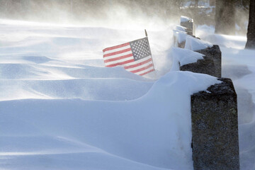 A United States of America flag flying at a veteran's gravestone during a record blizzard in 2015.; Mount Pleasant Cemetery, Arlington, Massachusetts.