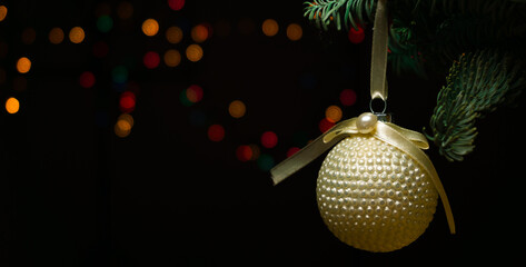 Hanging yellow Christmas ball on the Christmas tree on black background with orange bokeh lights. Christmas background, christmas card, banner on website.