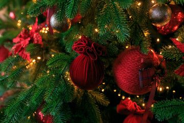 Closeup of red bauble hanging from decorated Christmas tree. Christmas, holidays and seasonal greetings concepts. copy space burgundy velvet balls on green pine branches. Festive christmas background.