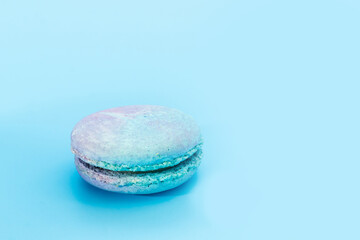 Blue French macaroon on light blue background. Tasty colourful macarons. Cookie made of two smooth halves, fastened with stringy fillings. French pastry made from egg whites. Culinary concept.